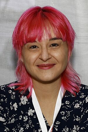 Portrait of Darcie Little Badger, a young Apache woman wearing a bandana, standing behind a wall of hanging cloths