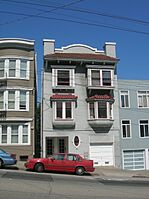 Photo of a gray three-story townhouse with red-tiled roofs on a sloped street