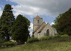 The stone tower of a church seen from the east, with a pyramidal roof, standing between trees.