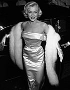 Photograph of a blonde woman wearing a glamorous dress, a fur scarf, and gloves