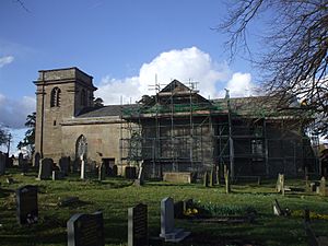 A plain stone church seen from the south, with a tower on the left, and scaffolding covering the transept in the middle and the chancel to the right