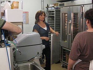 Christine Cushing standing in a commercial kitchen holding a baking tray, speaking