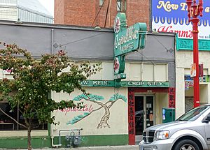 Photograph of a building's exterior with a doorway, mural of a tree, and a neon sign
