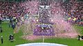 Confetti rains around a platform in the middle of a football pitch