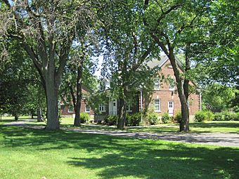 two brick buildings visible at different angles through trees; a walking path crosses in front