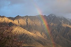 Rainbow in front of the Remarkables with patches of evening sunlight
