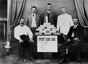 Group of men gathered around a table stacked with gold ingots from the Content Mine, Croydon, 1912