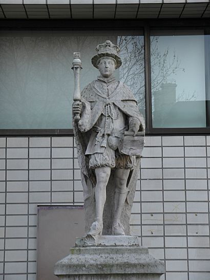 A stone statue of Edward VI. Edward wears a crown and holds a parchment in his left hand and a sceptre in his right hand. The king stands on a stone plinth.