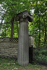 A large grey stone Ionic column and fence