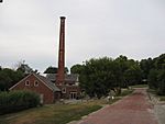 View of a red-brick path, with a red-bricked mill that has chimney stack built in its centre to the side of the path