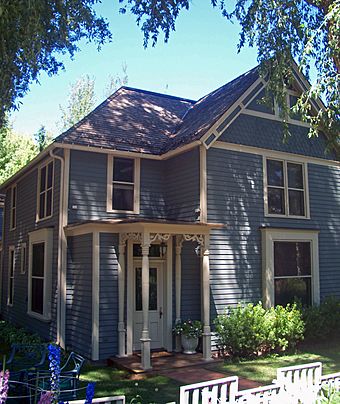 A blue wooden house with cream-colored trim, a pointed roof and a small porch with decorative wooden trim
