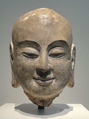 Sculpture of head of smiling monk with East Asian traits, part of limestone sculpture