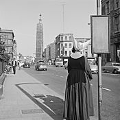 Nun with a most remarkable veil head dress waiting for a bus outside the Rotunda Hospital on Parnell Street, Dublin