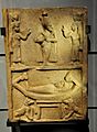 A mummy rests on a sacred boat guarded by Anubis. Above, figures of Osiris, Isis, and Nephthys. Sandstone stela. From Egypt, 332 BCE to 395 CE. Kelvingrove Art Gallery and Museum, Glasgow, UK