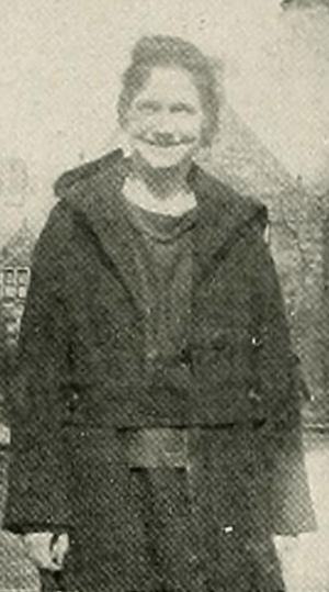 A smiling young white woman standing outdoors, wearing a dark coat