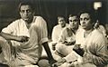 Photograph of Satyajit Ray seated with Ravi Shankar with several others in the background 