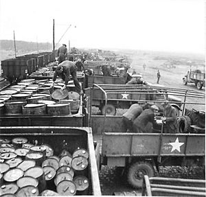Drums of oil being transferred from a train to Army lorries at No. 8 Army Railhead