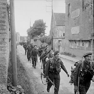 Royal Marine Commandos attached to 3rd Division for the assault on Sword Beach move through Colleville-sur-Orne on their way to relieve forces at Pegasus Bridge, Normandy, 6 June 1944. B5067