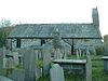 The north side of stone church with a slate roof, seen through a graveyard. There are two windows, a protruding vestry and, at the right, a bellcote