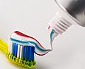 Photo with a blurry background and toothpaste from a tube of toothpaste being applied to the bristles of a toothbrush in the foreground