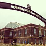View of a steel black-coloured archway with the words Fort York Armoury written in the centre of the arc. The exterior of the armoury is visible in the background