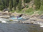 Canoers run rapids on a boulder-strewn river in the mountains.