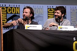 Matt Duffer on the left, with Ross Duffer on the right, both seated behind a table with name cards in front of them and looking to the viewer's left, with a San Diego Comic-Con BBanner in the background
