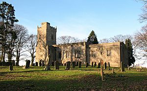 A stone church seen from a slight angle, with an embattled tower on the left, the nave in the centre, and the chancel on the right