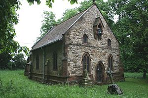 A plain stone church, seen from the southwest, with a bell hanging from a gabled bracket on the west wall