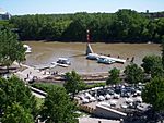 A muddy river floods a wooded urban area with boat docks and riverside seating.