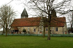 A stone church with red tiled roofs seen from the south, showing the chancel, the south aisle and porch, and the tower with a pyramidal roof