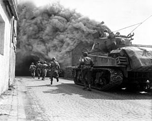 United States Army soldiers supported by a tank move through a smoke filled street in Wernberg, Germany during April 1945