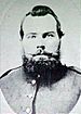 Head of a heavy-set white man with a beard and pointed mustache, wearing a military jacket.