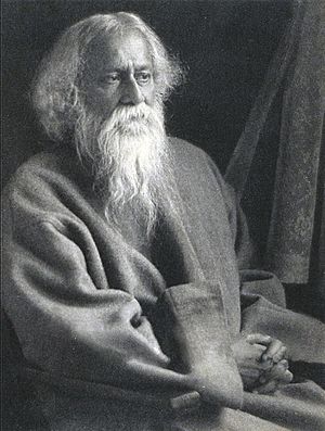Late-middle-aged bearded man in Grey robes sitting on a chair looks to the right with serene composure.