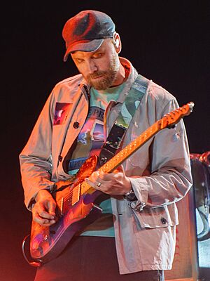 Buckland on stage with his guitar, wearing a black hat and beige jacket