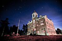 An old, two-story brick courthouse with third-story bell tower under a starry night sky.
