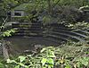 Semicircular stone steps, partially obscured by trees. Water to the left