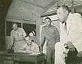 In a "war room", three military men watch a worried man in civilian dress