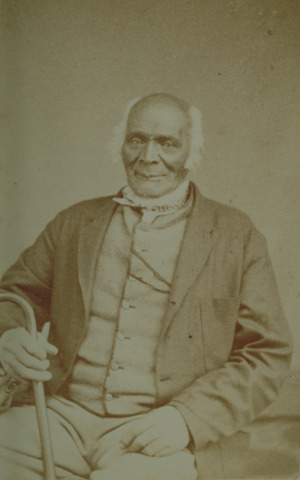 Studio portrait of an elderly African-American man wearing a coat and vest and holding a cane