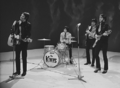 The rock band The Kinks in a TV show performance. From left to right are a singer/electric guitarist, a drummer behind a small drumkit, and two guitarists.