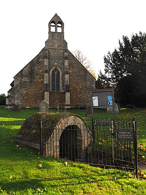 A thatched, stone church seen from the west showing two large buttresses with a window between and a double bellcote above