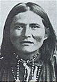 Head of a Native American man with straight shoulder-length hair, wearing a beaded necklace tight around his neck.