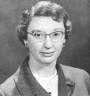 A middle-aged white woman with short side-parted wavy hair, wearing glasses and a suit jacket