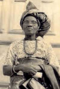 Photo of Funmilayo Ransome-Kuti standing with hands clasped together in front of her