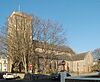 A long, flint-built church with a tall squared-off tower in the foreground, seen from close proximity.