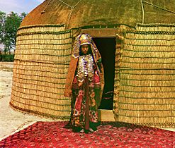 Woman in traditional dress and jewelry standing on rug in front of yurt Service-pnp-ppem-01300-01324v