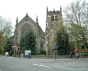 A stone church seen from the west; on the left is the nave with a large Perpendicular window, and on the right is the tower with corner pinnacles