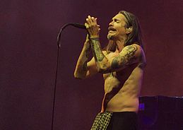 A man singing, his arm tattoos visible