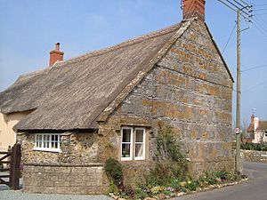 Old stone building with thatched roof on road junction.