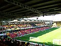 A two-tiered seating area featuring red, yellow and black seats, running along the length of a football pitch.